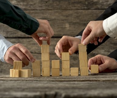 Hands of five businessman holding wooden blocks placing them int