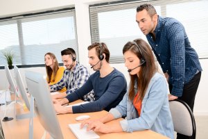 group of four young people with desktop computer in row and headset training with teacher instructor in customer service call support helpline business center