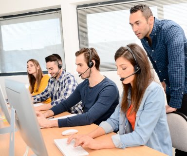 group of four young people with desktop computer in row and headset training with teacher instructor in customer service call support helpline business center