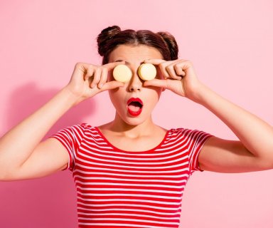 Close-up portrait of nice cute charming attractive glamorous lovely funny comic teen girl in striped t-shirt covering eyes with colorful delicious snack opened mouth isolated over pink background