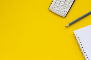 Calculator, notepad and pencil on a yellow background, space for text